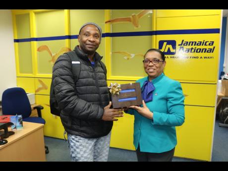 Arnett Pryce (right), member service representative, JN Bank UK Representative Office presents Stanhope Gibbs, a JN member with a 'Braata box' as part of the organisation's 'Celebrate our Jamaican Heritage Promotion'. Gibbs received an authentic token that was made by a social enterprise in Jamaica for opening a JN Bank Savings Account .
