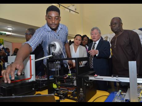 André Craig, of the Department of Mechanical Engineering, explains the use of his 3D printer to Gary ‘Butch’ Hendrickson (second right), chairman and CEO of Continental Baking Company; Martin Henry (right), UTech administrative manager; and Tiffany Wong, special projects officer of Continental, at the opening ceremony of Research, Technology & Innovation Day on Thursday. 