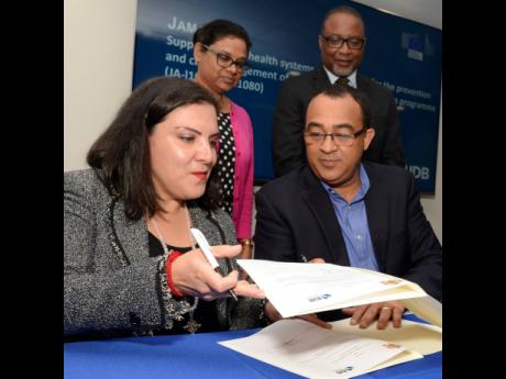 Health Minister Dr Christopher Tufton (right, seated) and Adriana La Valley (left, seated), chief of operations at the Inter-American Development Bank in Jamaica, exchange documents during a contract signing for a US$100-million loan to upgrade the public health sector yesterday.  Looking on are Chief Medical Officer Dr Jacquiline Bisasor-McKenzie  and Dunstan Bryan, permanent secretary in the Ministry of Health. The ceremony took place at the IDB’s offices in Kingston.