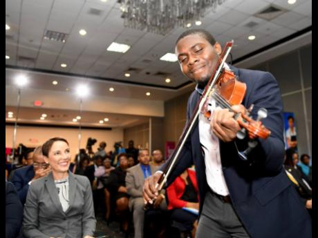 Foreign Affairs Minister Kamina Johnson Smith looks on while Michael Wilson plays the violin at the launch of the eighth Biennial Jamaica Diaspora Conference at The Jamaica Pegasus hotel yesterday. The conference will be held from June 16-20 at the Jamaica Conference Centre.