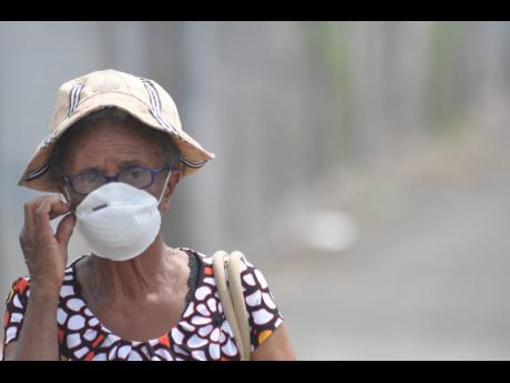 A senior citizen covers her nose with a dust mask in Duhaney Park due to smoke caused by a fire at the Riverton City dump on Saturday, March 14, 2015.