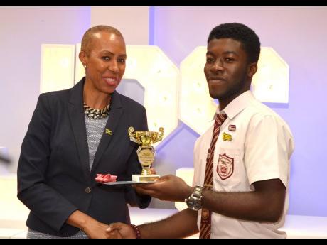 Science, Energy and Technology Minister  Fayval Williams (left), presents a trophy and $20,000 bursary to Herbert Morrison Technical High School student, Sherwin Williams, who was awarded for outstanding performance in the 2018 Caribbean Secondary Education Certificate (CSEC) industrial technology examination. The presentation was made during an awards ceremony hosted by the Jamaica Public Service Foundation for top students in the 2018 examination, at Hotel Four Seasons in Kingston on April 16. 