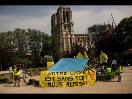 People fix a banner that reads in French: ‘Notre-Dame is roofless, we too!’ during a protest in front of the Notre Dame cathedral in Paris yesterday. 