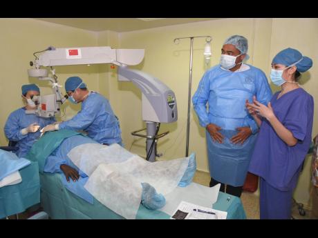 Health Minister Dr Christopher Tufton (second right) listens attentively to a member of the Chinese Bright Journey Eye Care Mission technical team, Dr Xi Chen, as they observe a cataract surgery being conducted by members of the mission at the Kingston Public Hospital last week.