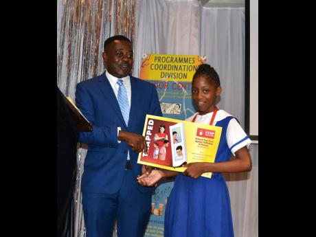 Nicolette Williams is presented with a calendar  by DSP Carl Berry, head of the Anti-Trafficking in Persons Unit, during the HUSH: Children Symposium held at the Institute of Jamaica yesterday. Berry sought to open the children’s eyes to dangers lurking in society, including in cyberspace, as countries try to tackle human trafficking.