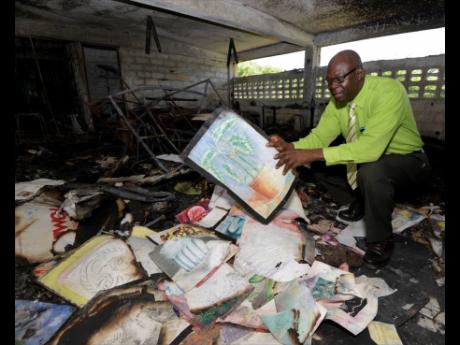 Calbert Thomas, principal of Seaforth High School in St Thomas, salvages what remains of works done by visual arts students at the school after fire destroyed the department earlier this month. 