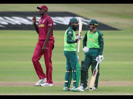 West Indies captain Jason Holder (left) walks past South Africa’s Hashim Amla (centre) raising his bat to celebrate scoring 50 runs during their Cricket World Cup warm-up match in Bristol, England, yesterday. On the right is South Africa’s Quinton de Kock. 