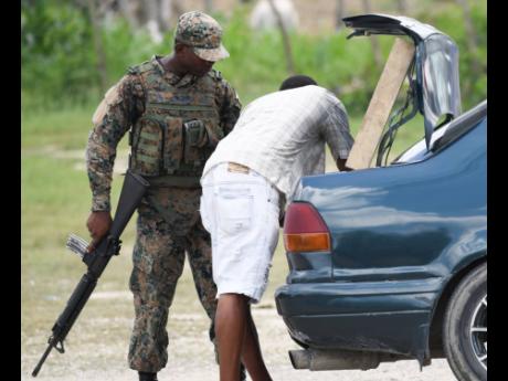 A soldier conducts a search of a vehicle at a checkpoint in Whitehouse, Westmoreland, which is one of three parishes, including Hanover and St James, under a state of public emergency. The security measure restricts personal freedom and grants extraordinary powers to soldiers and the police. 