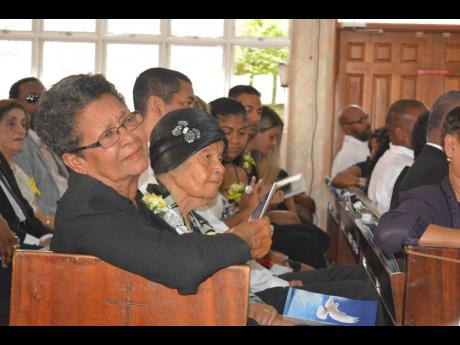 Mrs. Novelette Tai listens attentively to tributes paid to her late husband, Aston. Beside her is Tai’s sister, Cynthia.