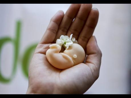 A woman holds a fetus doll in the palm of her hand. 