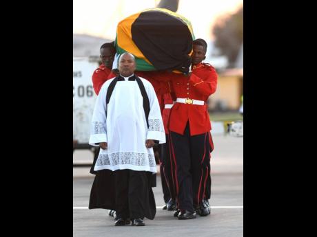 Lt Col Denston Smalling, chaplain of the Jamaica Defence Force, leads members of the 1st Batallion Jamaica Regiment as they carry the coffin bearing the remains of former Prime Minister Edward Seaga, which arrived at Norman Manley International Airport yesterday evening. Seaga, 89, passed away last week at a Florida hospital in the United States.