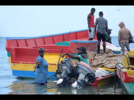 Fisherwoman Shernette Douglas (left) gets assistance from other fishermen in Rocky Point, Clarendon, to load and prepare her boat for sea yesterday.