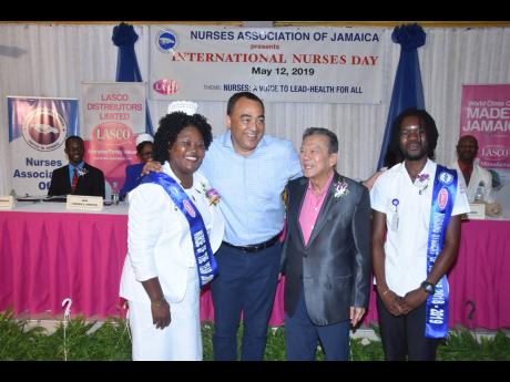 Minister of Health and Wellness Dr Christopher Tufton (second left) embraces founder and executive chairman of LASCO Affiliated Companies, Lascelles Chin (second right), and LASCO/Nurses Association of Jamaica (NAJ) Nurse of the Year 2018-2019 Denese Dacres Reeves during the NAJ/LASCO International Nurses’ Day media launch on May 12. Looking on is LASCO/NAJ Nursing Student of the Year 2018-2019 Desmond Campbell Jr.  