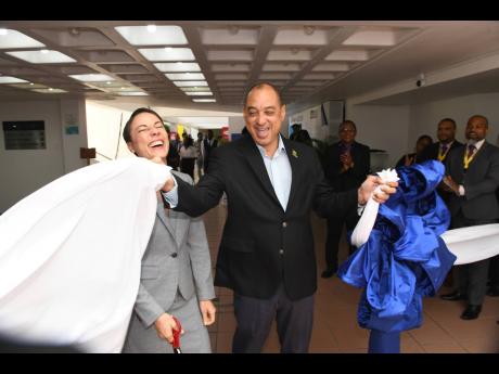 Minister of Foreign Affairs and Foreign Trade Senator Kamina Johnson Smith reacts as Senator Don Wehby, chairman of the 8th Biennal Jamaica Diaspora Conference, assists by ripping the cloth at the ribbon-cutting ceremony to officially open the marketplace at the Jamaica Conference Centre yesterday.
