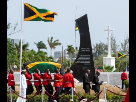Members of the 1st Battalion Jamaica Regiment carry the coffin bearing the body of Edward Seaga past the monument memorialising his great political arch-rival, Michael Manley, at National Heroes Park yesterday afternoon. Gladstone Taylor/Multimedia Photo Editor