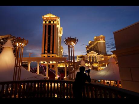 In this January 12, 2015 file photo, a man takes pictures of Caesars Palace hotel and casino in Las Vegas. Eldorado Resorts will buy Caesars in a cash-and-stock deal valued at $17.3 billion, creating a casino giant. The acquisition on Monday, June 24, puts about 60 casinos and resorts in 16 states under a single name, one of the biggest gambling and entertainment ventures in the United States. 