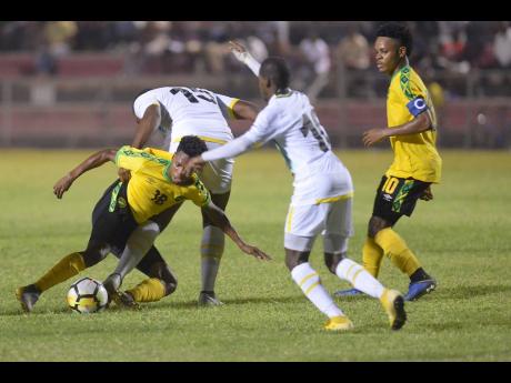 Jamaica’s Nicque Daley (left) goes to ground after being tackled by Dominica’s Peltier Kassim during their CONCACAF Under-23 Qualifier at the Anthony Spaulding Sports Complex in Kingston on Wednesday. Jamaican Alex Marshall (right) looks on. The game ended 1-1.