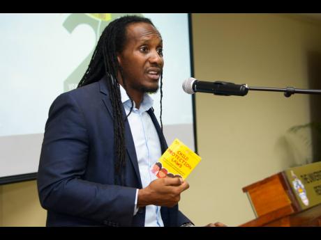 Junior Youth Minister Alando Terrelonge holds a copy of the Children Protection Laws pocket booklet while speaking at a child protection seminar and booklet launch at the UWI Regional Headquarters on Thursday.