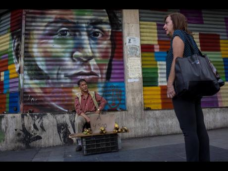 A street vendor sells bananas in front of a painting with the image of Venezuelan Independence hero Simón Bolívar, in Caracas, Venezuela,  on Tuesday, July 16.