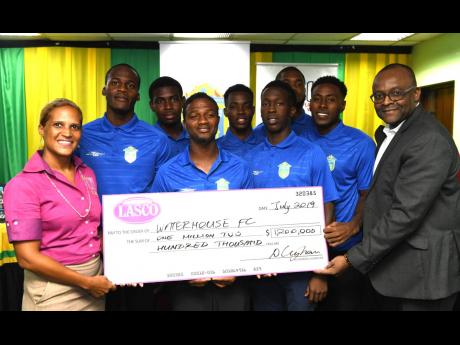 Danielle Cunningham (left), beverage marketing manager, LASCO Distributors, presents a cheque for $1.2 million to Donovan White (right), president of the Waterhouse Football Club, at yesterday’s media briefing ahead of the Scotiabank Concacaf League match between Waterhouse and HS Herediano of Costa Rica. Sharing in the moment are Waterhouse head coach Marcel Gayle (fourth left) and several players of the club. The briefing was held at the offices of the Jamaica Football Federation.