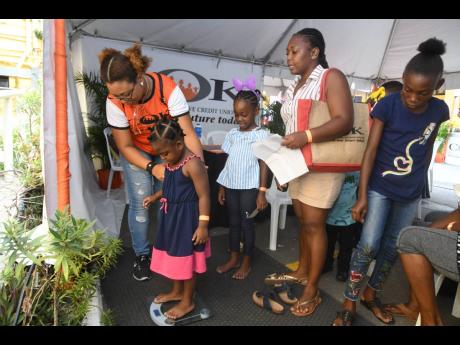 Nicole Shim (left), administrative assistant at COK, assists with weighing children of COK members for their back-to-school medicals. The COK’s back-to-school fair took place at the credit union’s Slipe Road, Kingston, offices on August 10. 