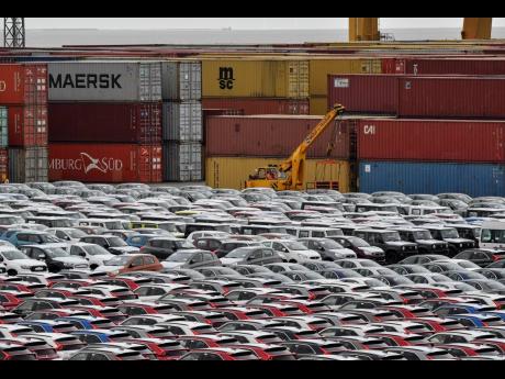 In this Thursday, May 16, 2019 file photo, cars for export and import are stored in front of containers at the port in Bremerhaven, Germany. In June 2019 German industrial production dropped significantly for the second time in three months and in July business confidence fell to a seven-year low.
