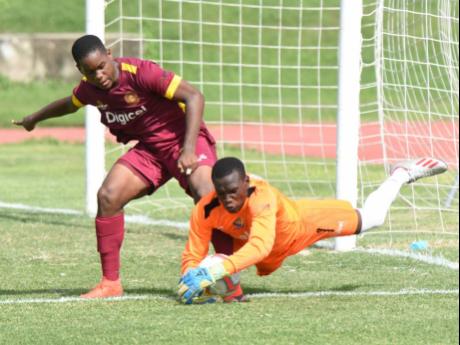 Tarrant High School goalkeeper Jonathan Currie lunges out to collect a loose ball while challenged by Wolmer’s Boys School’s Zhavier Lynch during their ISSA/Digicel Manning Cup game at the Stadium East field yesterday.