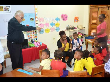 Minister with responsibility for Education, Youth and Information Karl Samuda (left) interacts with students at the Savanna-la-Mar Inclusive Infant Academy in Westmoreland during a tour on Friday, October 4. Looking on are teachers Dahlia Richards (seated) and Angella McKoy. 