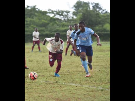 Herbert Morrison Technical High School’s Marc Graham (left) and Holland High’s Demar Chambers intensely chase the ball during their ISSA/WATA daCosta Cup match at the Holland High playing field on Monday, October 8, 2018. 