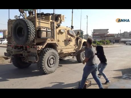 Residents who are angry over the US withdrawal from Syria hurl potatoes at American military vehicles in the town of Qamishli, northern Syria, yesterday. 