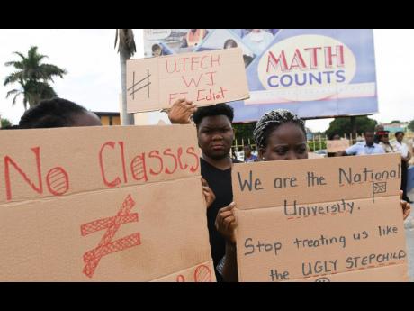 Placard-bearing UTech students protest at the entrance to the Ministry of Education’s Heroes Circle offices yesterday. 
