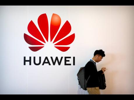 In this October 31, 2019 file photo, a man uses his smartphone as he stands near a billboard for Chinese technology firm Huawei at the PT Expo in Beijing. 