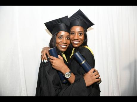 Shanece Roberts-Morgan (left) and twin sister Shannoya Roberts celebrate after the Caribbean Maritime University’s 39th graduation ceremony at the National Indoor Sports Centre last Friday. 