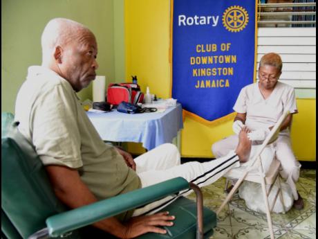 Dahlia Brown, senior footcare assistant, World Walk Foundation, Jamaica Chapter, checks the feet of Milton Melbourne, a resident of the Denham Town Golden Age Home, during a Rotary Club of Downtown Kingston health fair at the home on Tuesday, November 12.