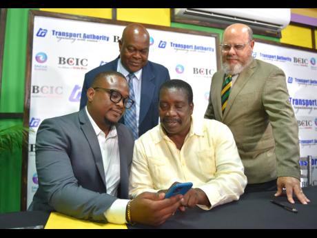 Minister of Transport and Mining Robert Montague (seated at right) looks at a training application with Chief Executive Officer of EduFocal Business Limited Gordon Swaby during a signing ceremony at the ministry’s office in Kingston on Thursday. Observing are Cecil Morgan (standing at left), managing director of the Transport Authority; and Managing Director of British Caribbean Insurance Company Peter Levy.