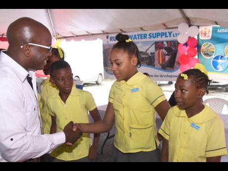 Minister without Portfolio in the Ministry of Economic Growth and Job Creation, Pearnel Charles Jr (left), shakes hands with water monitor at Essex Hall Primary School Asheiba Chung (second right), at the official handover of a new rainwater harvesting system at  the institution in West Rural St Andrew last week. Nicholas Green (left) and Amoy Marshall, who have also been appointed water monitors, look on. The system was installed by the Rural Water Supply Limited, which is an agency under the ministry.​