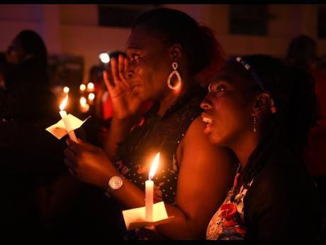 Althea Cohen (left) breaks down beside Kemesha Gabriel as they participate in the annual candelight vigil at Holy Cross Roman Catholic Church yesterday in remembrance of a friend they lost to HIV/AIDS. Yesterday was commemorated as World AIDS Day.