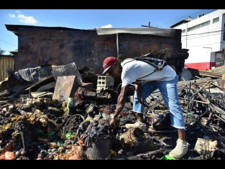 Delroy McFarlane, who lost all his goods, is devastated as he picks through the rubble at the May Pen Market on Monday. The market was gutted by fire on Sunday.
