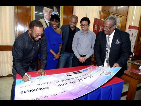 Professor Ian Boxill affixes his signature to a symbolic cheque, as filmmakers Vennessa Hanshaw, Kaiel Eytle and Hanif James, along with Professor Dale Webber, pro-vice-chancellor and principal of The UWI, Mona, look on.