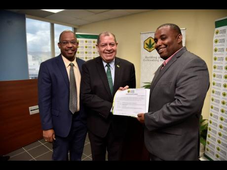 Minister of Industry, Commerce, Agriculture and Fisheries Audley Shaw (centre) hands over the Cannabis Licensing Authority’s (CLA) 50th licence for operations in the local medical cannabis industry to director of Outlier Biopharma Limited, Brian Thelwell (right), on Wednesday) at the CLA’s New Kingston offices. Sharing in the moment is Chief Executive Officer, CLA, Lincoln Allen. 