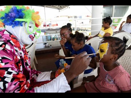 A clown paints the face of a student  with special needs during the Sanmerna Foundation Annual Christmas Treat which was held at the Half-Way Tree Transport Centre in St Andrew.