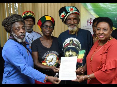 Culture Minister Olivia Grange (right) hands over the copy of the deed for the Coral Gardens Trust Fund to members of the Rastafari Coral Gardens Benevolent Society on Thursday. The members are (from left) Lewis Brown, Edward Fray, Pamella Williams and Isaac Wright. The deed was signed at a ceremony at the culture ministry in New Kingston.