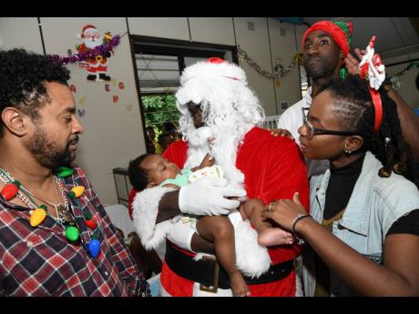 
Orville ‘Shaggy’ Burrell (left) stands by as Santa Claus holds baby Keora Hibbert while Skorcha and Andrei Roper, brand manager for Restaurants of Jamaica, look on during the Shaggy Christmas treat at the Bustamante Hospital for Children in Kingston last Tuesday. 