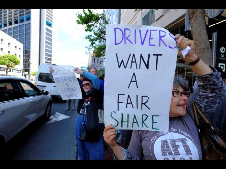 In this May 8, 2019 photo, Uber and Lyft drivers carry signs during a demonstration outside of Uber headquarters in San Francisco. A California law that makes it harder for companies to treat workers as independent contractors takes effect next week.
