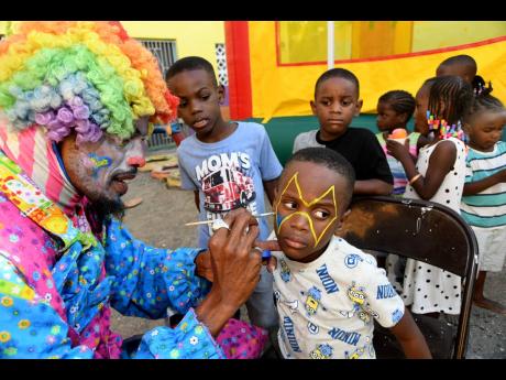 A clown painting the face of children at the Faith United Church of God 10th Annual Christmas Treat, put on by the Gift of Love Foundation, Ara Party Rentals and Dr Alfred Dawes, at the church located in the Mandela Terrace Community, St Andrew, on Sunday.