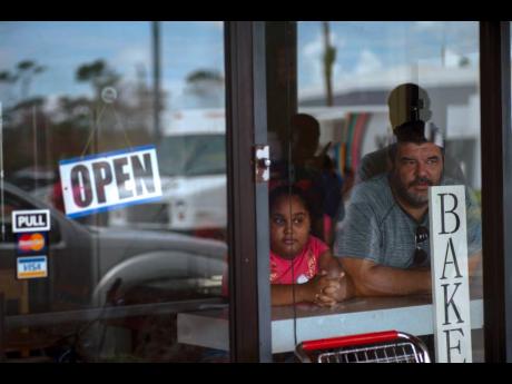 A man and girl peer out from a bakery and cafeteria in Freeport, Bahamas, on September 11 last year. Like the bakery, Bahamas remained open for business despite the ravaging impact of Hurricane Dorian. 