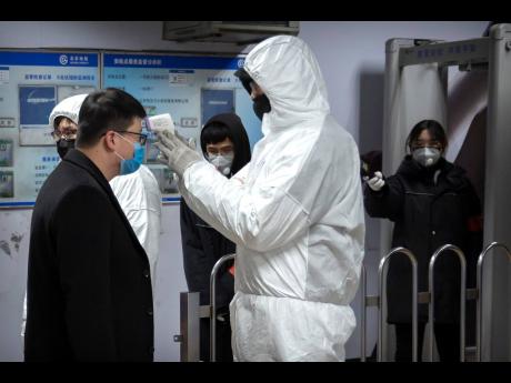 A worker wearing a hazardous materials suit takes the temperature of a passenger at the entrance to a subway station in Beijing yesterday. 