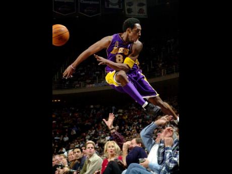 In this December 2001, file photo Los Angeles Lakers’ Kobe Bryant jumps over a row of fans after saving the ball from going out of bounds in the second half of the Lakers 107-101 win over the Houston Rockets in Houston.
