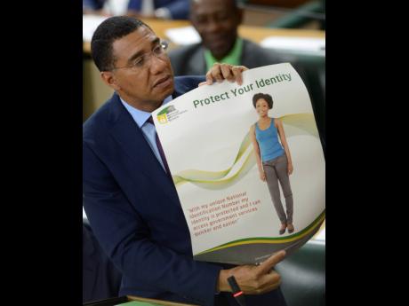 Prime Minister Andrew Holness shows a poster printed for NIDS during a sitting of Parliament on Tuesday, May 14, 2019. The Holness administration has made the identification system an important objective during its term of office. 