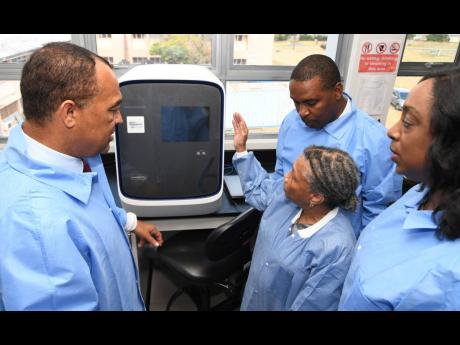 Dr Christopher Tufton (left), minister of health and wellness, listens as Dr Monica Smikle (second right), head of the National Influenza Centre, discusses the capacity of a coronavirus testing machine during a tour of the facility at The University Hospital of the West Indies yesterday. Looking on are Dr Michelle Hamilton (right), acting director of the National Laboratory Services, and Dr Carl Bruce, medical chief of staff and consultant neurosurgeon of UHWI.